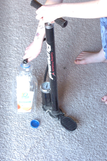 A child pumping up the jug using a bicycle pump.